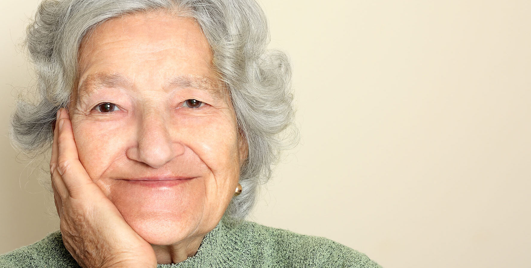 A close-up image of an older lady smiling. She has her chin rested on her hand.